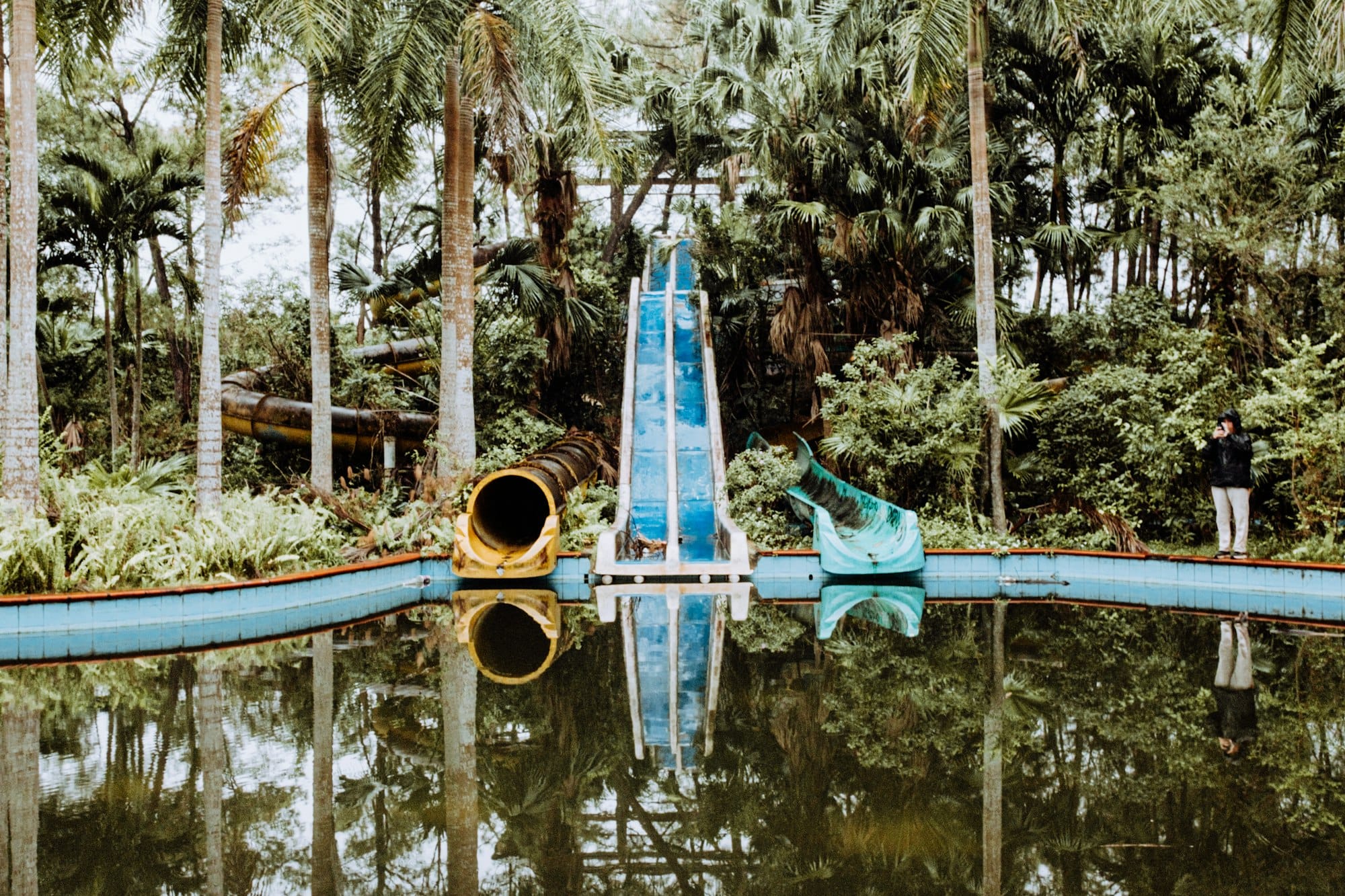 Abandoned water slides reflect in a pool.