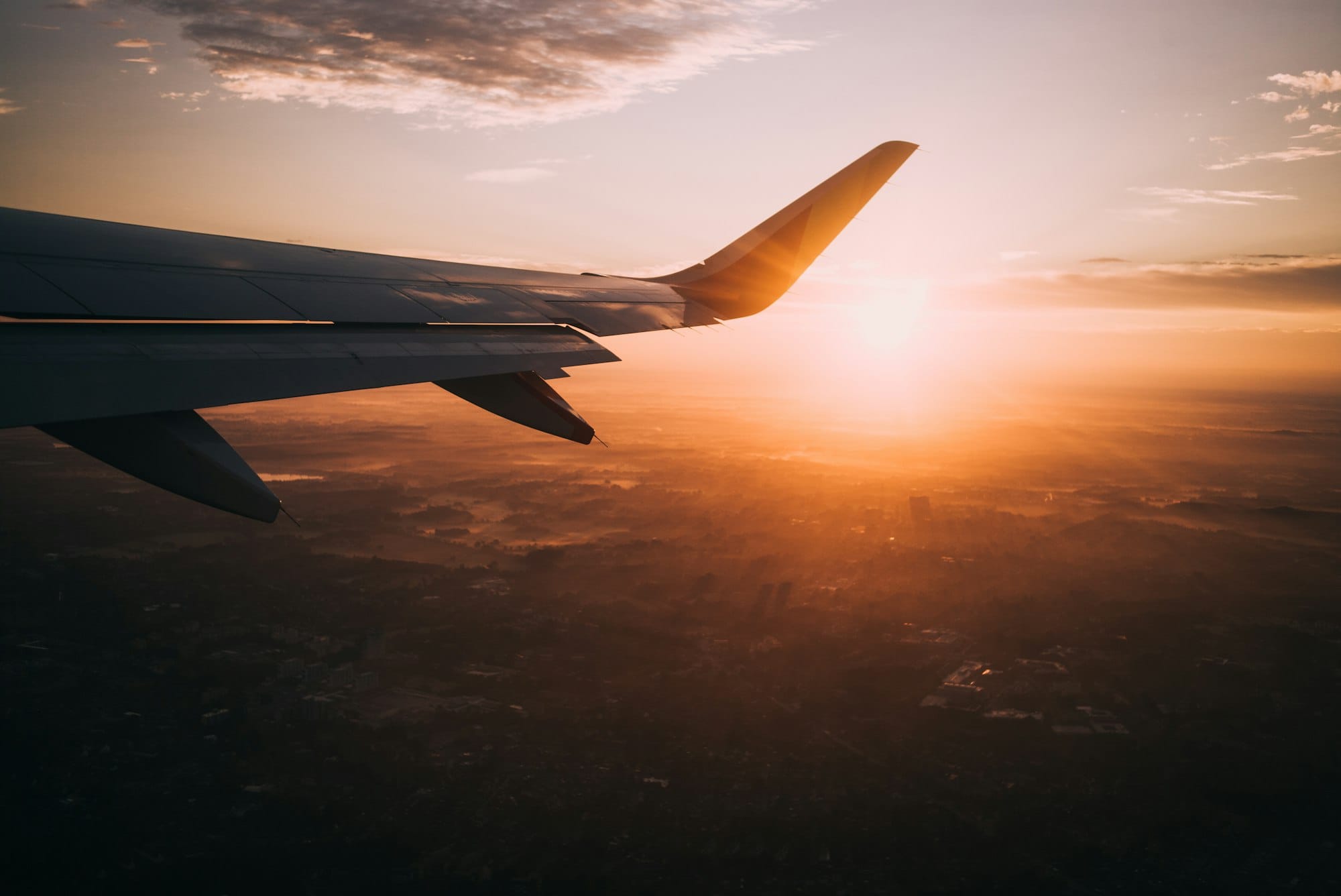 Airplane wing seen from a window seat as the sun rises over farmland and clouds