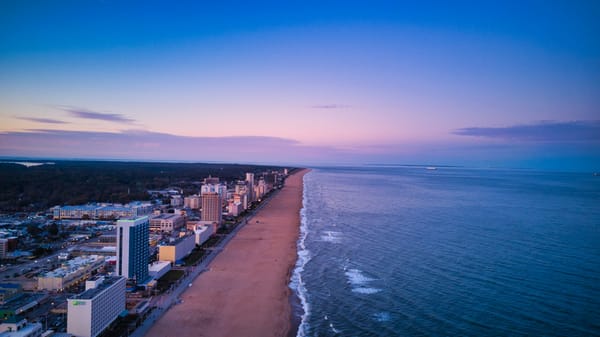 Aerial view at dusk of a long sandy beach lined with oceanfront hotels beside calm Atlantic water